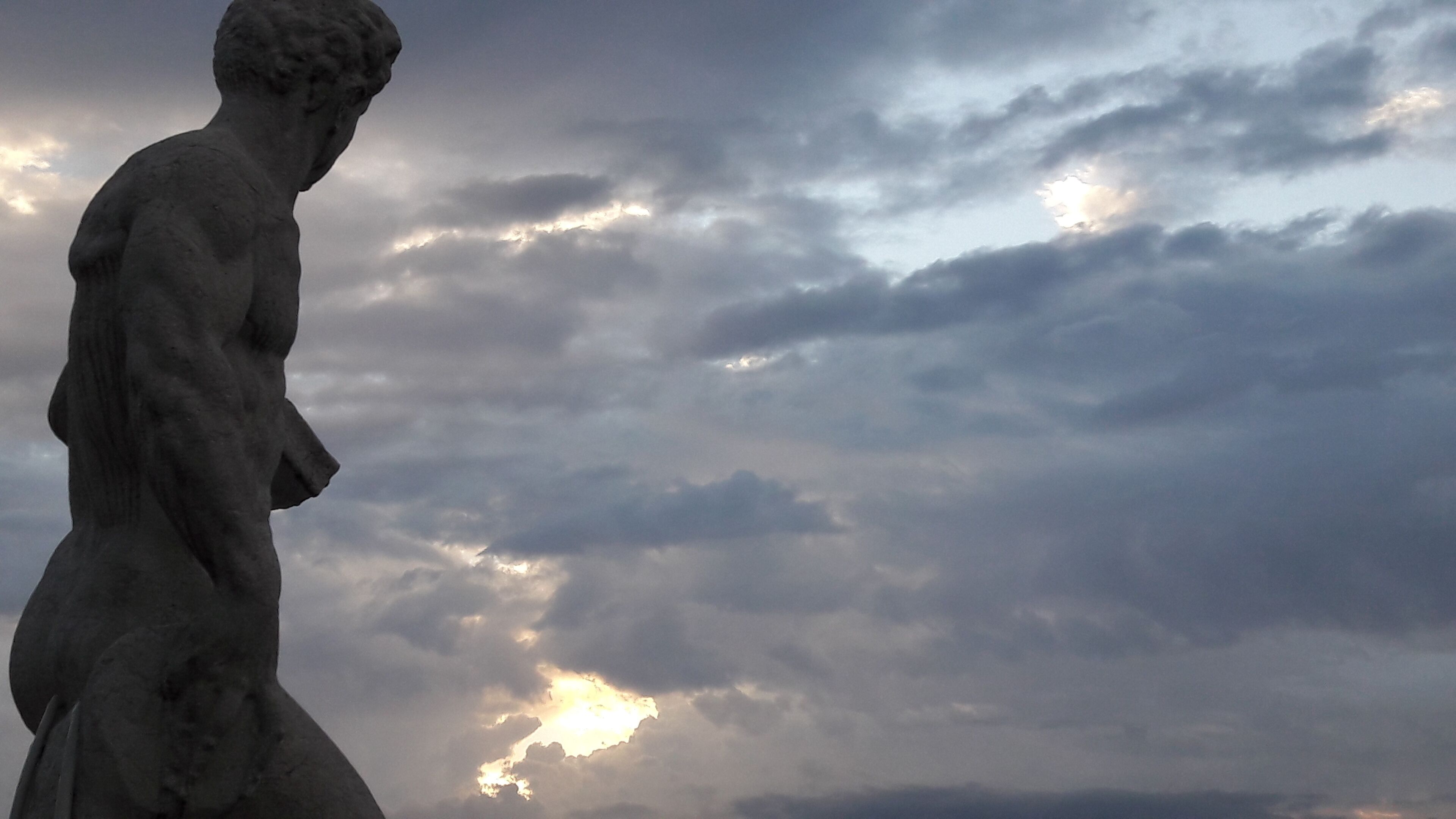 A statue of a classical figure against a cloudy sky.