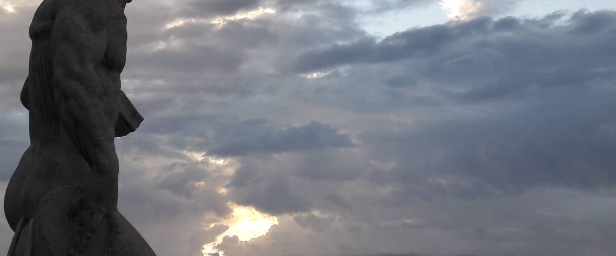 A statue of a classical figure against a cloudy sky.