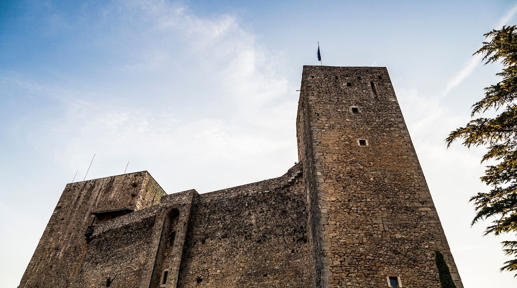 A tall, historic stone tower with a pointed roof, surrounded by clear blue sky and sparse clouds.