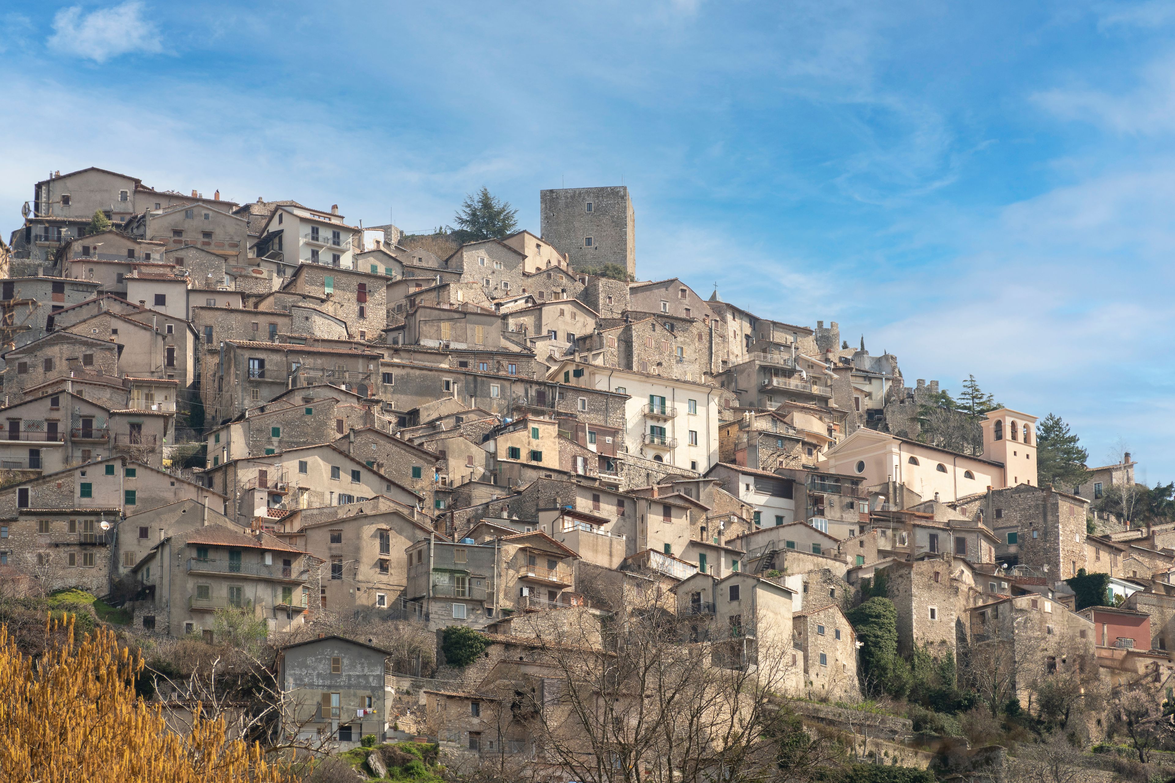 A densely packed hillside town with historic stone buildings and a prominent tower.