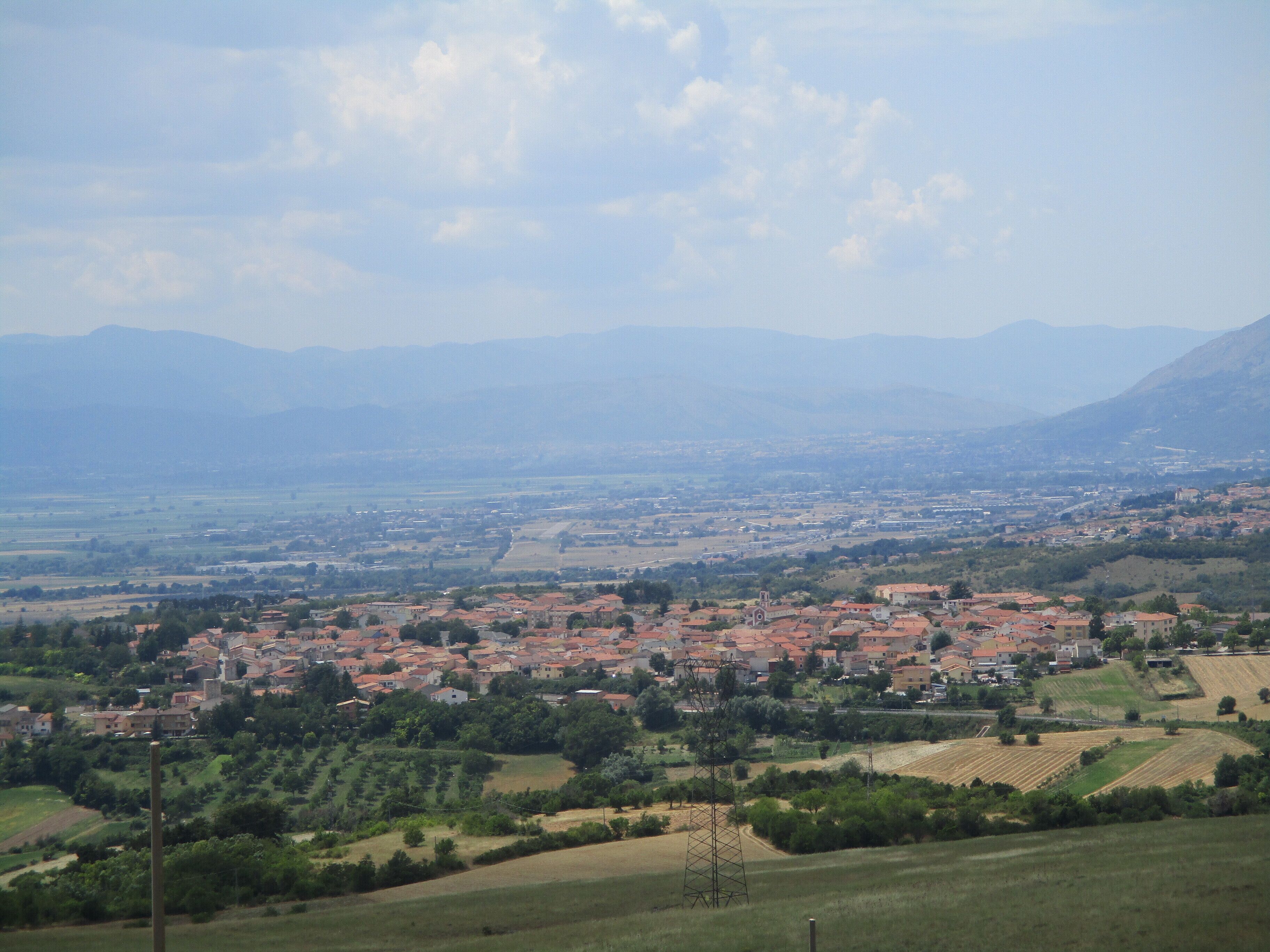 A rural landscape with a town, fields, and mountains in the background.