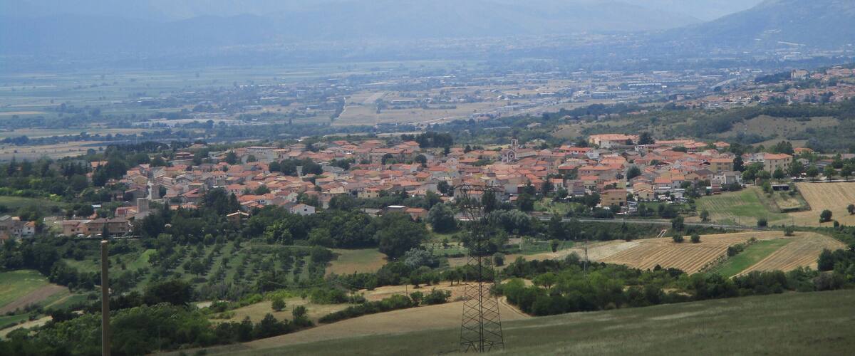 A rural landscape with a town, fields, and mountains in the background.