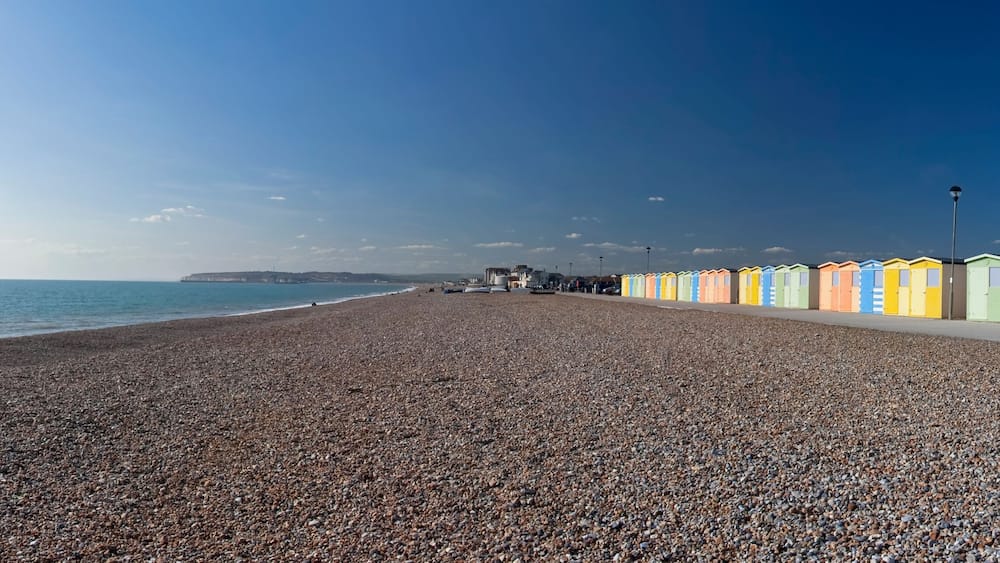 A pebbled beach with colorful beach huts and a clear sky.