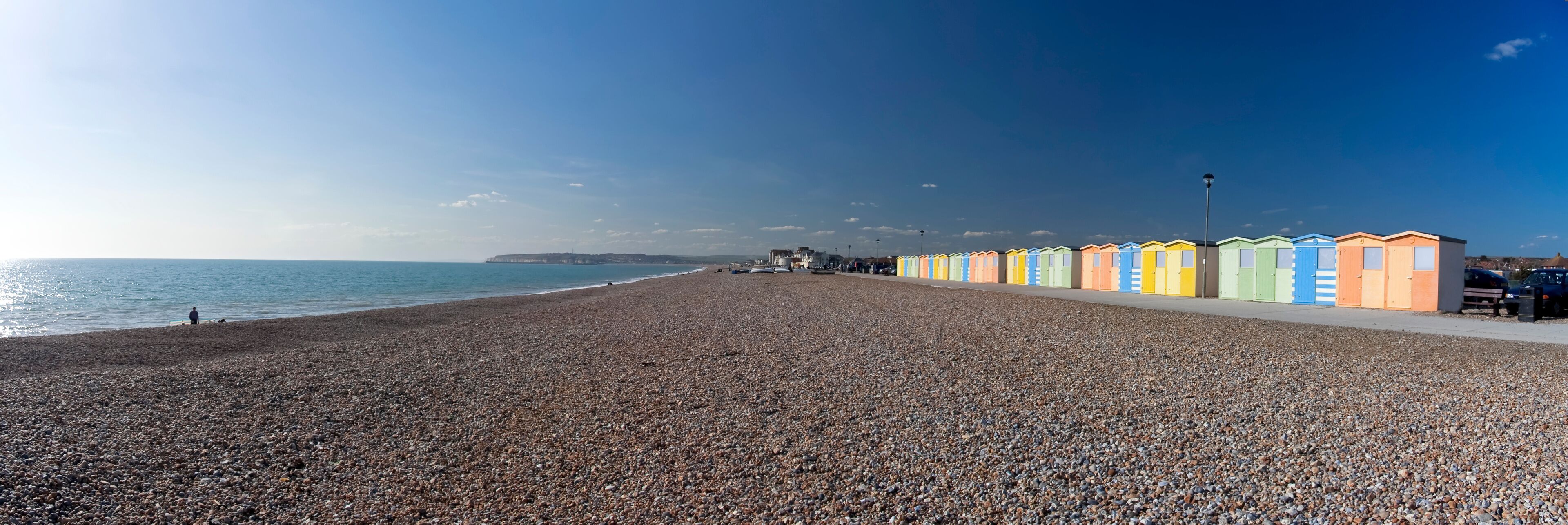 A pebbled beach with colorful beach huts and a clear sky.