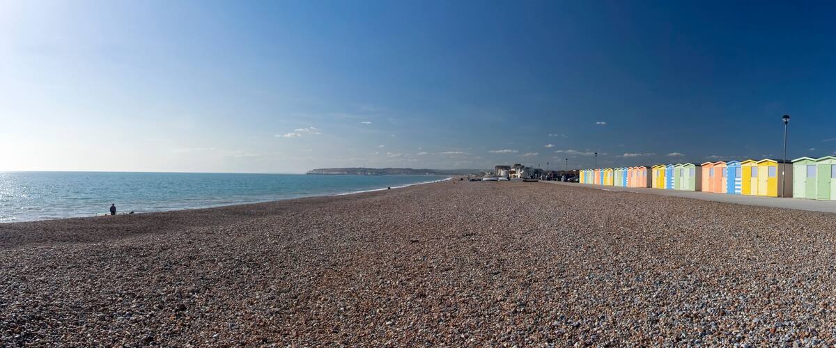 A pebbled beach with colorful beach huts and a clear sky.