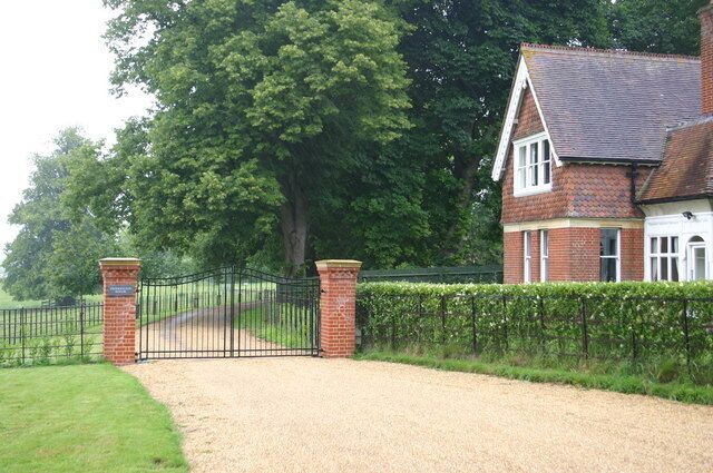 A gated driveway leading to a brick house with a white door, surrounded by a hedge and trees.
