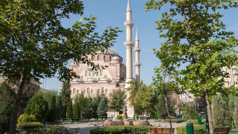 Une mosquée dotée de deux minarets, entourée d’arbres et bordée de bancs dans un parc.