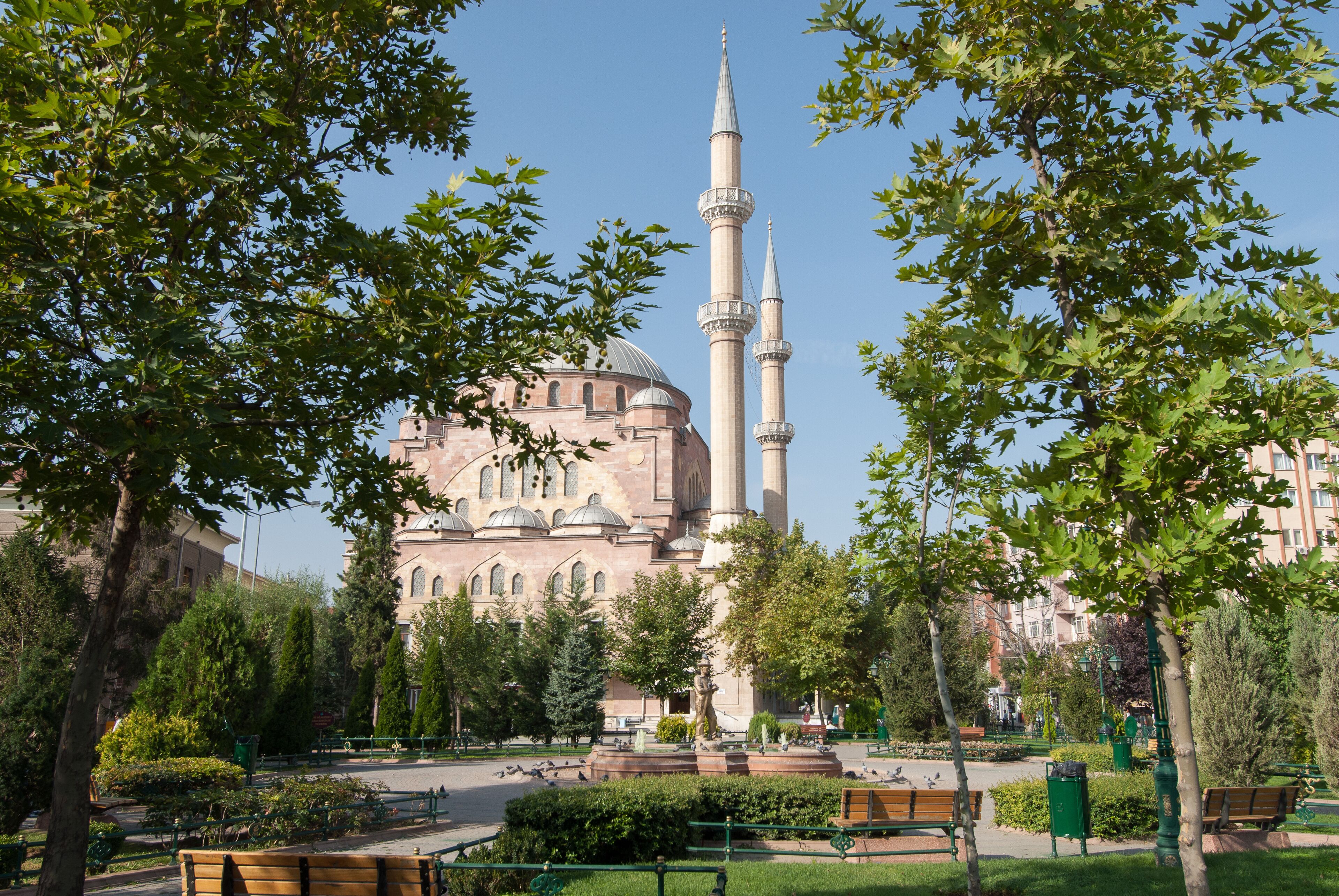 A mosque with two minarets surrounded by trees and benches in a park.