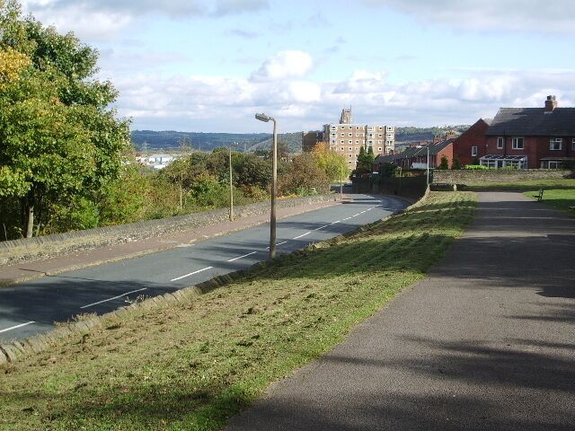Una calle con aceras, árboles y edificios al fondo.