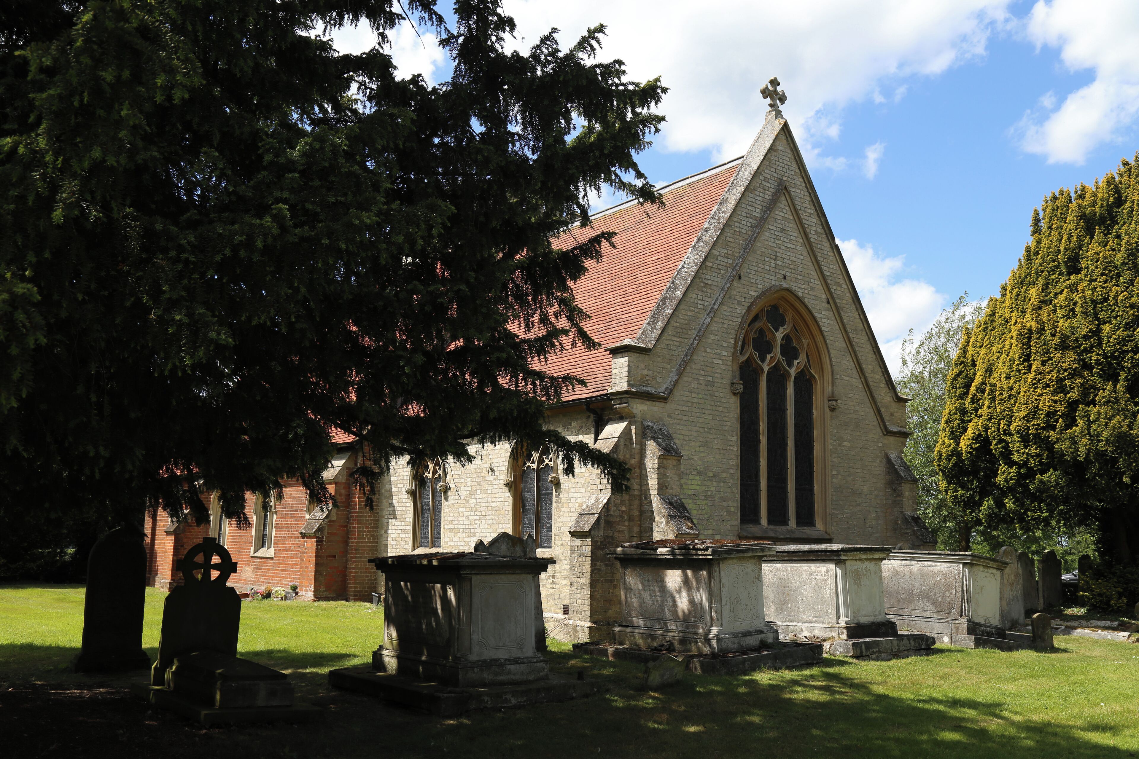 St Germain's Church, Bobbingworth, Essex, England - chest tombs and graves under a yew tree against the buttressed chancel east wall, from the south-east