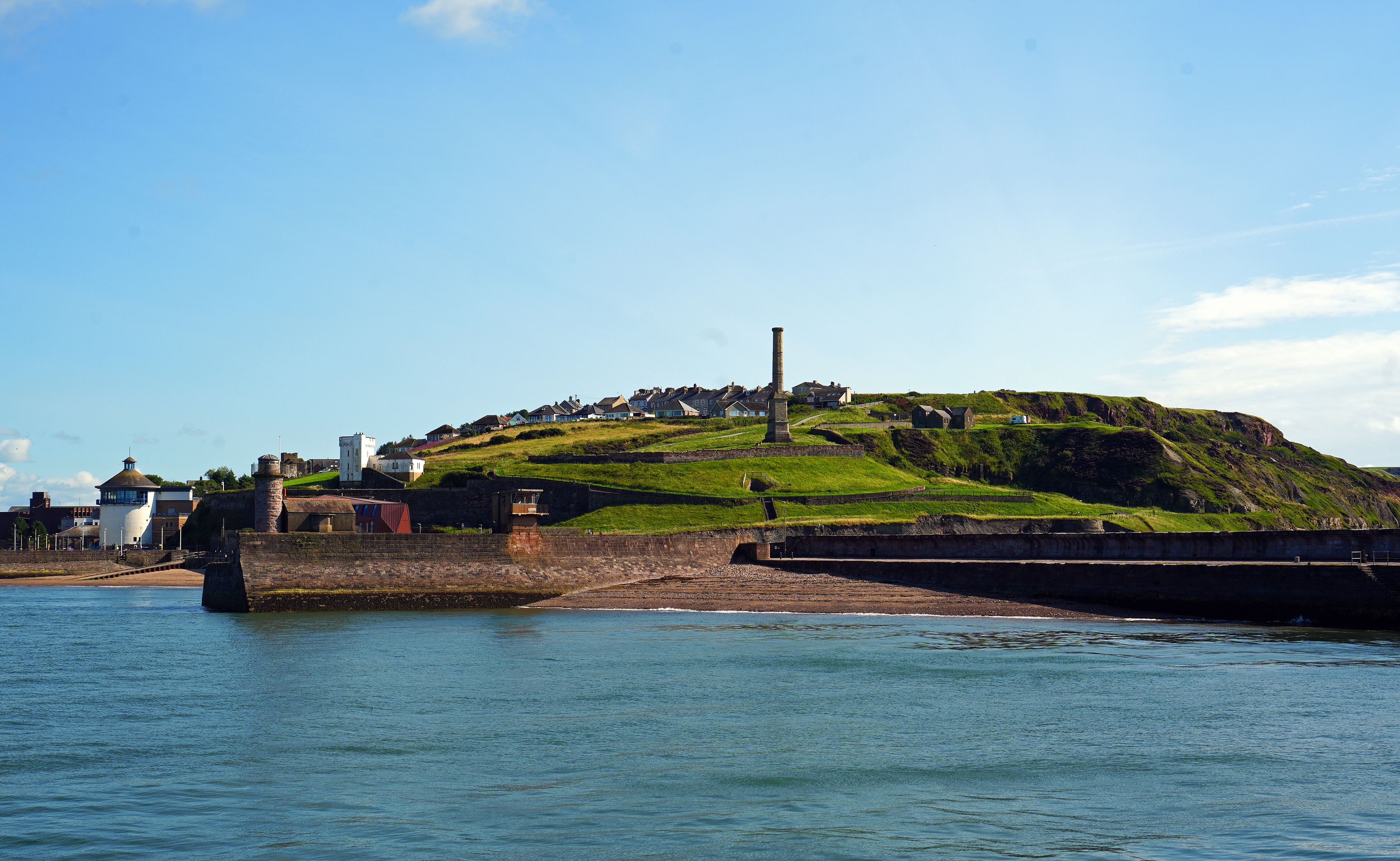 A coastal landscape with a hill, a lighthouse, and a pier.