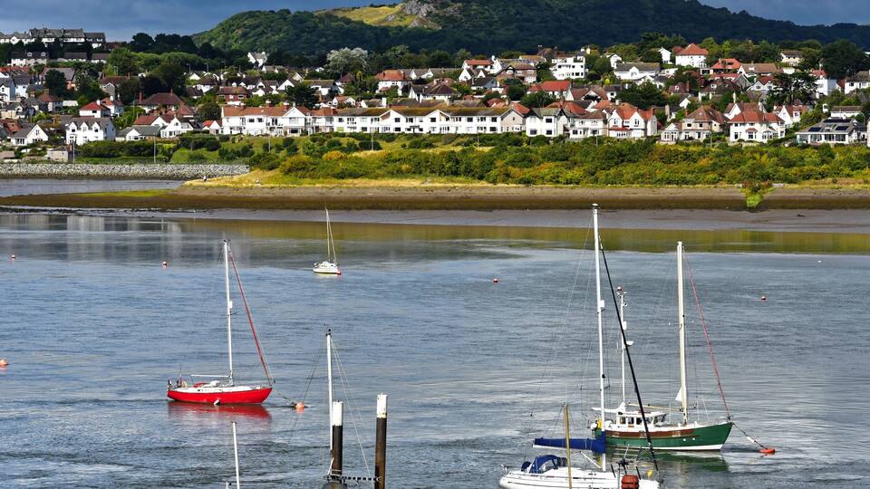 A harbor with several sailboats, a sandy beach, and a town with houses in the background.