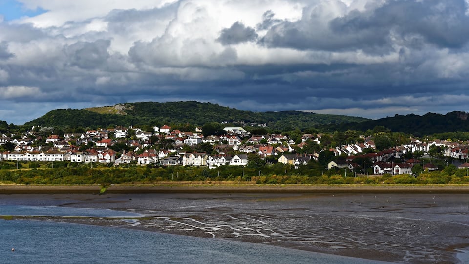 A coastal town with houses on a hillside, a beach, and a cloudy sky.