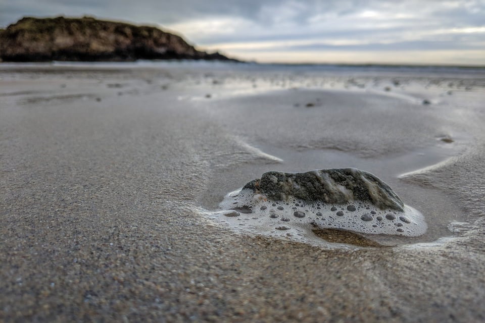 A pebble beach with a large rock in the foreground and a distant rocky outcrop.
