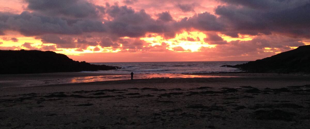 A beach at sunset with dramatic clouds and silhouettes of hills.