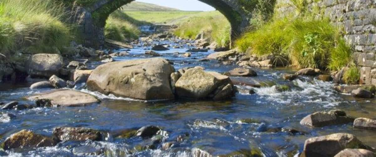 A stone bridge over a flowing river with rocks and grass on either side.