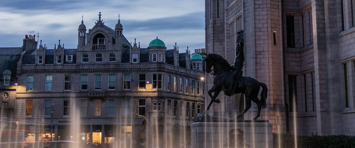 Un edificio histórico con arquitectura detallada y una estatua de un jinete y su caballo en primer plano.