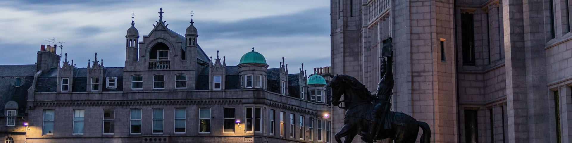 A historic building with intricate architecture and a statue of a horse and rider in the foreground.