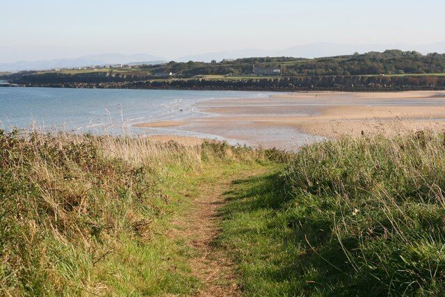 A coastal path leading to a beach with a clear view of the sea and distant hills.