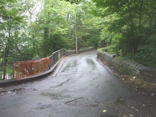 A wet road with a metal guardrail and stone wall on a forested path.