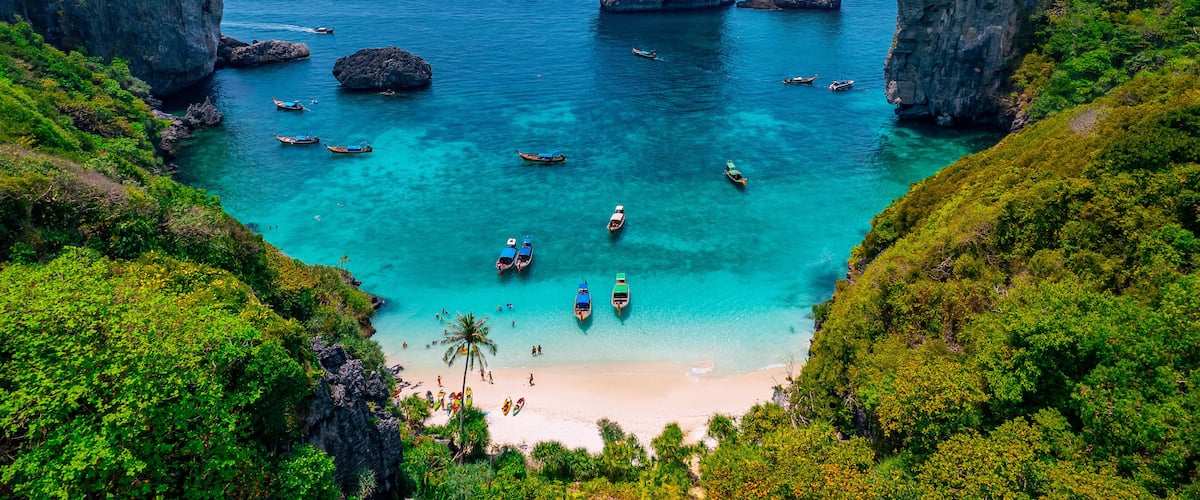 A coastal landscape with clear turquoise waters, boats, and prominent rock formations.