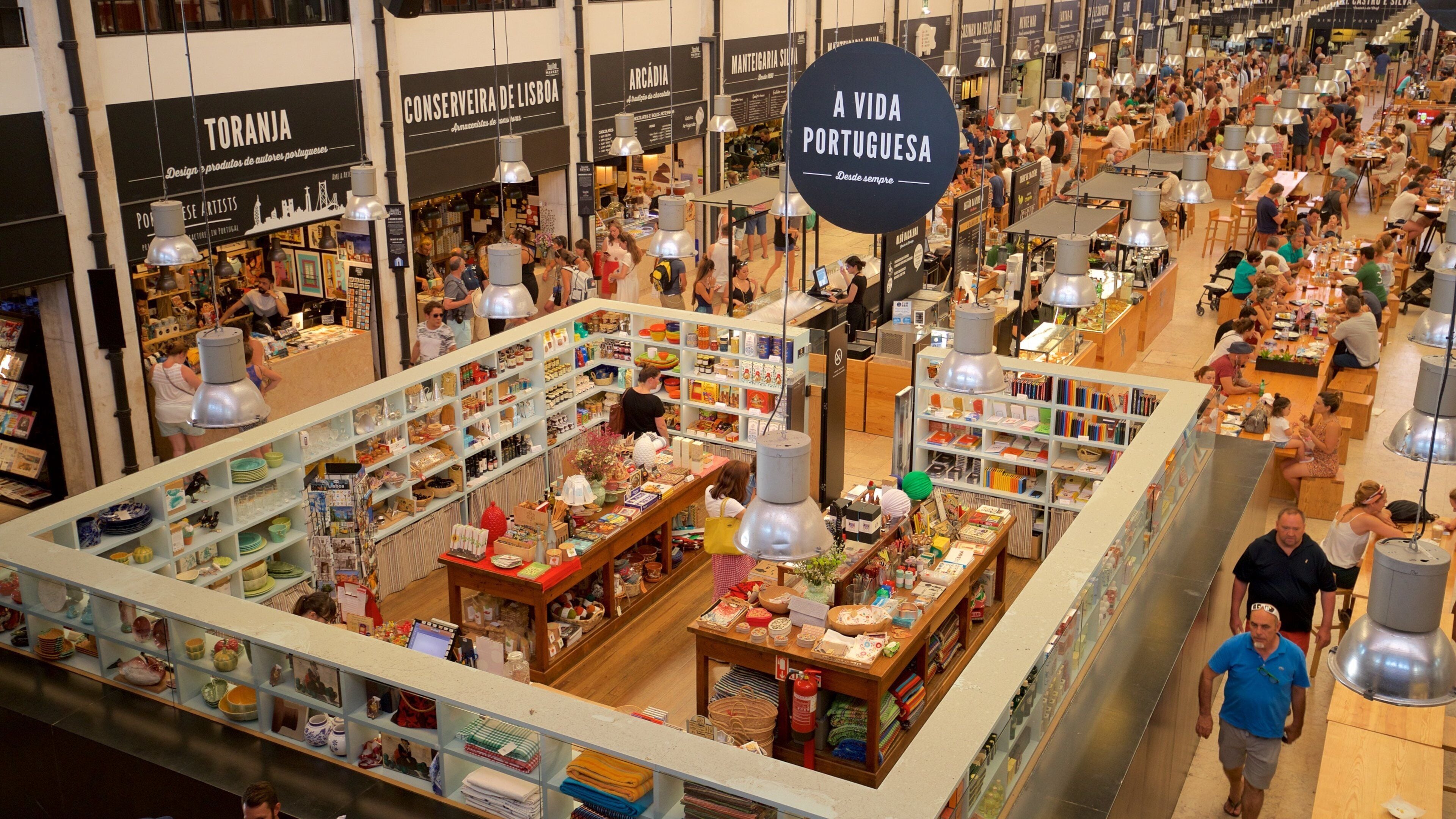 A busy indoor market with various stalls selling food, books, and crafts.