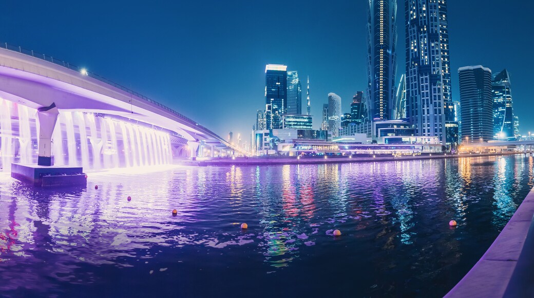 Illuminated waterfall bridge in downtown Dubai at night with thousands of small lights on high skyscrapers. Popular tourist attractions in UAE
