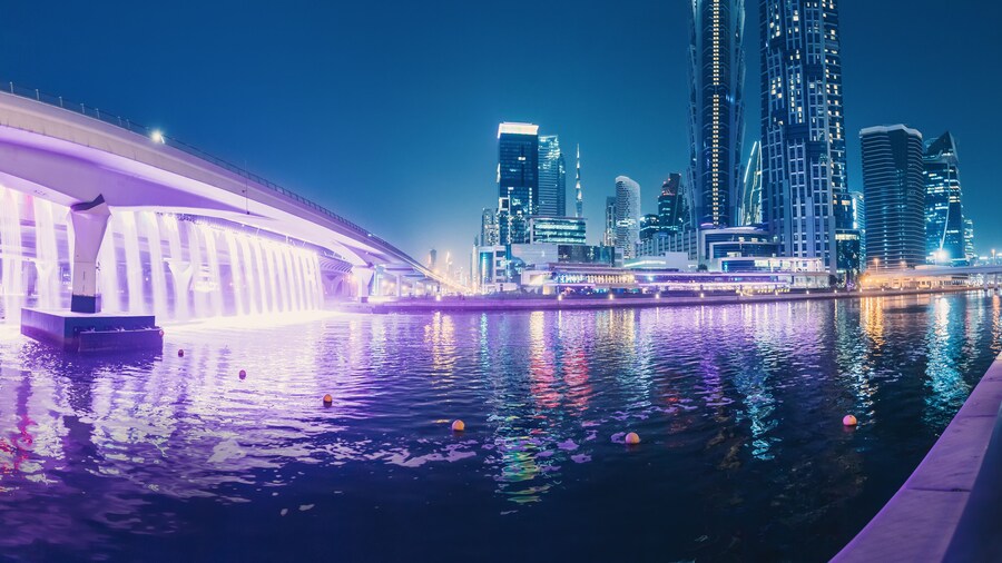 Illuminated waterfall bridge in downtown Dubai at night with thousands of small lights on high skyscrapers. Popular tourist attractions in UAE