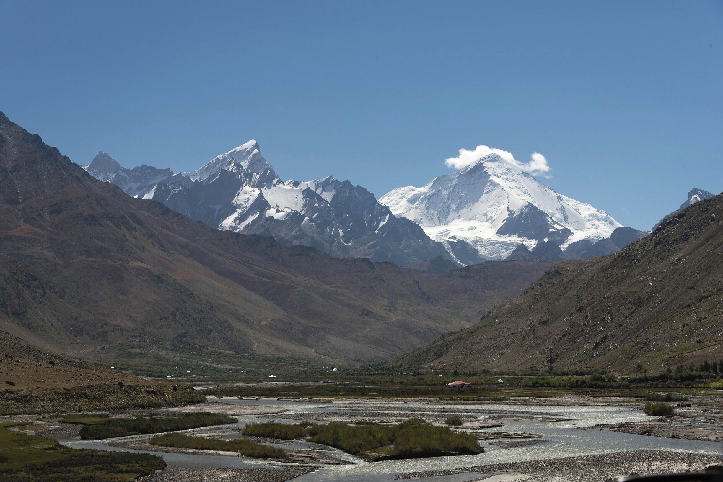 A mountainous landscape with a snow-capped peak in the center, a river flowing through a valley, and rugged terrain on either side.