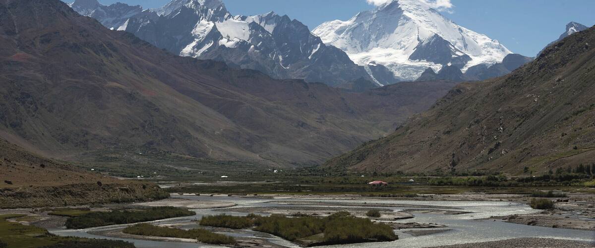 A mountainous landscape with a snow-capped peak in the center, a river flowing through a valley, and rugged terrain on either side.