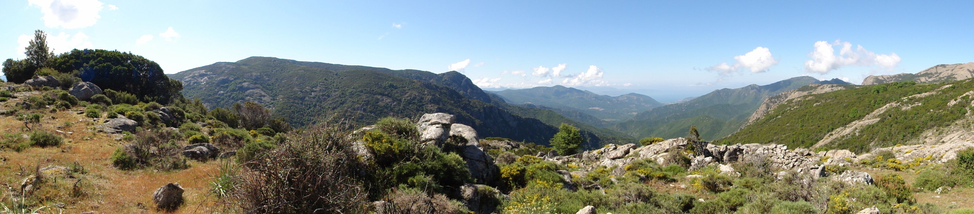 A mountainous landscape with rocky terrain, sparse vegetation, and distant hills under a clear sky.