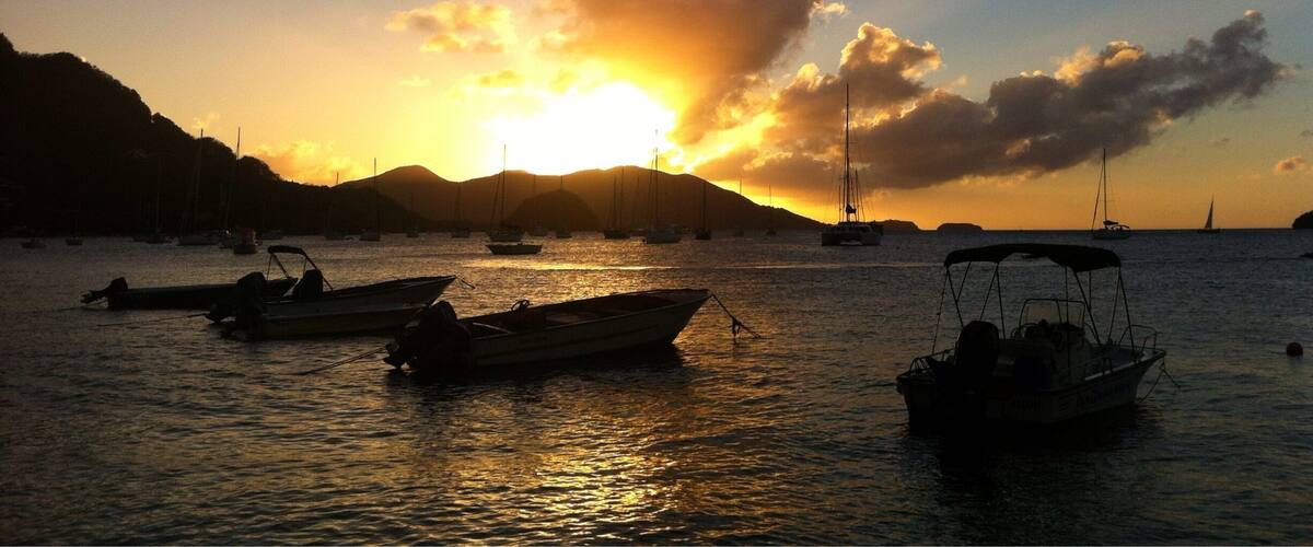 A sunset over a calm sea with several boats anchored.