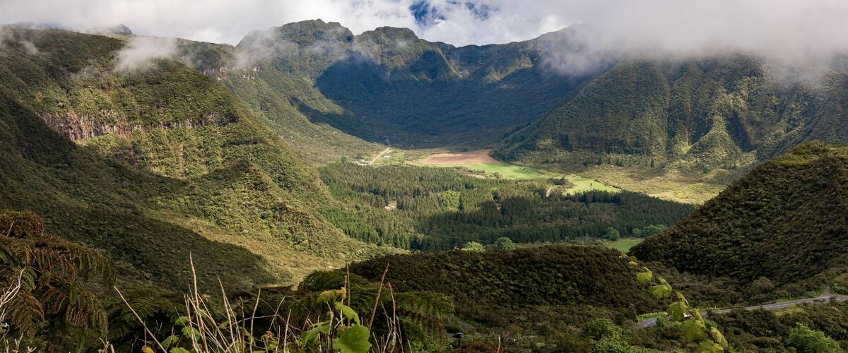A valley with lush green hills, a winding road, and a mountain range in the background.