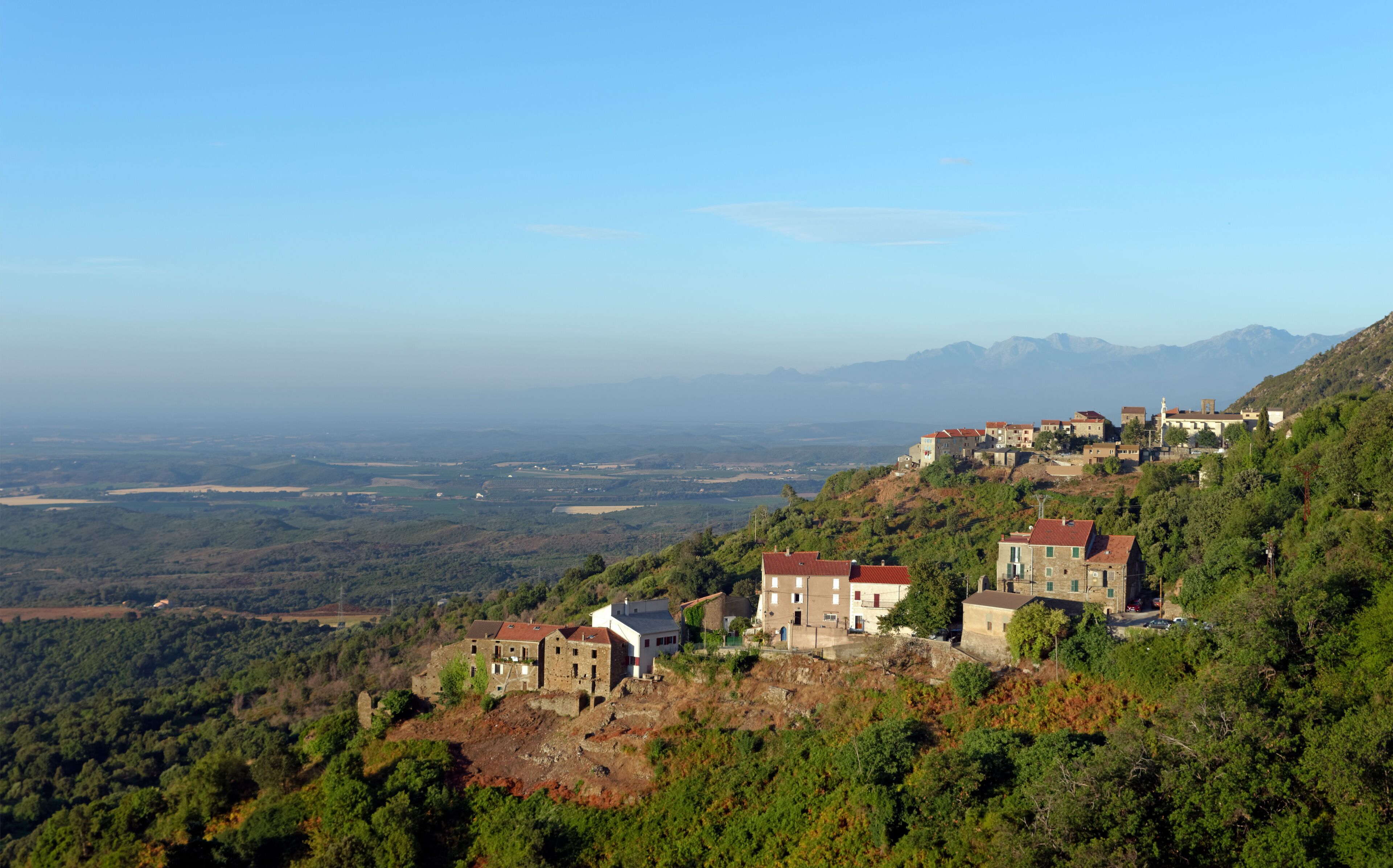 A hillside village with traditional stone buildings and a view of the valley below.