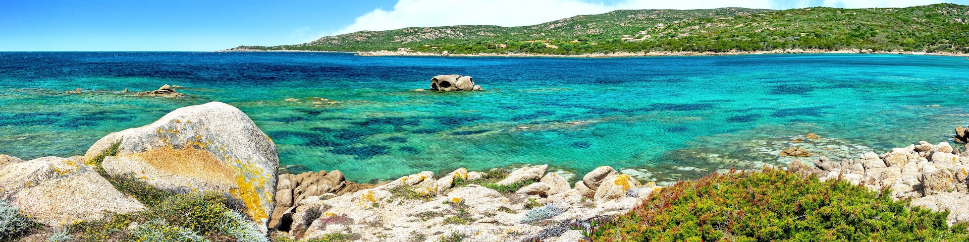 Un paisaje costero con aguas turquesas cristalinas, costas rocosas y colinas verdes al fondo.