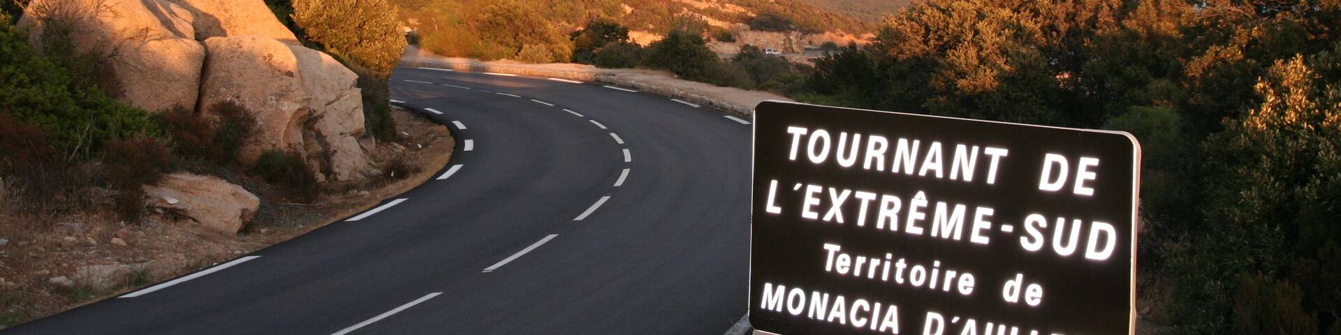 A winding road with a sign indicating the Tournant de L'Extrême-Sud, a scenic route in the Monacia d'Aullene territory.