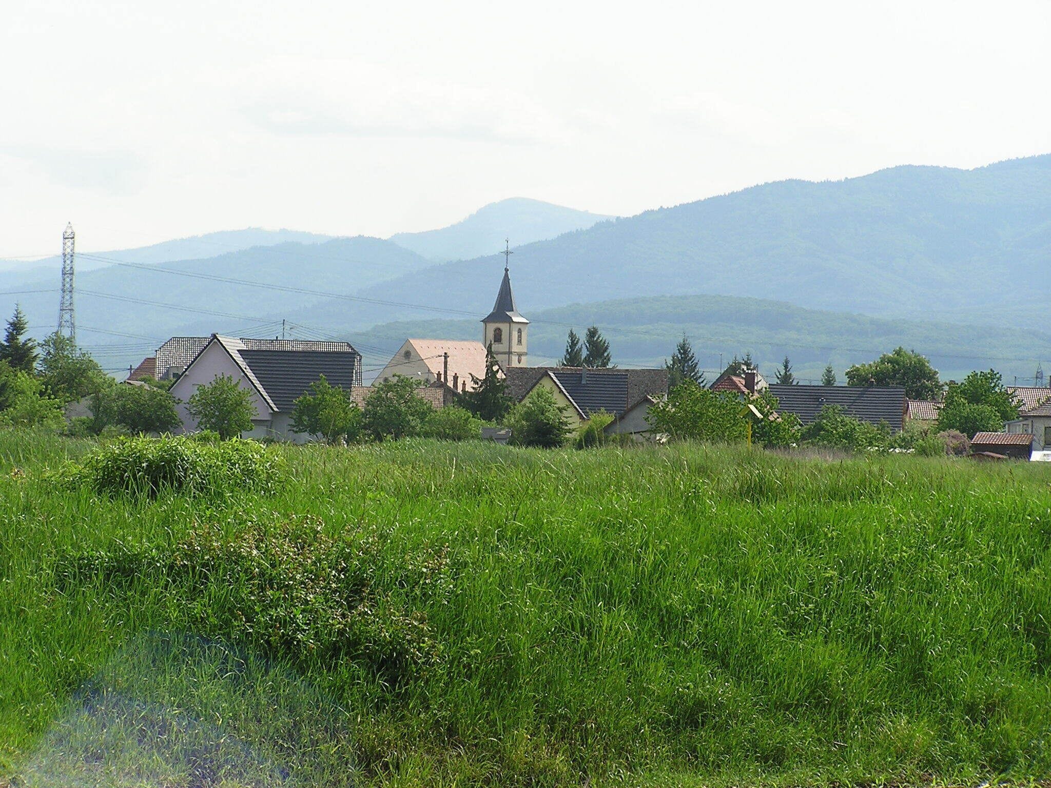 A rural village with houses, a church, and mountains in the background.