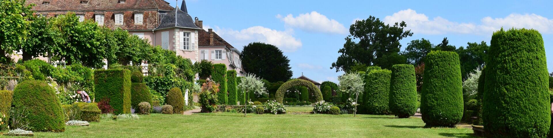 A large, historic house with a well-manicured garden, including neatly trimmed hedges and a variety of trees.