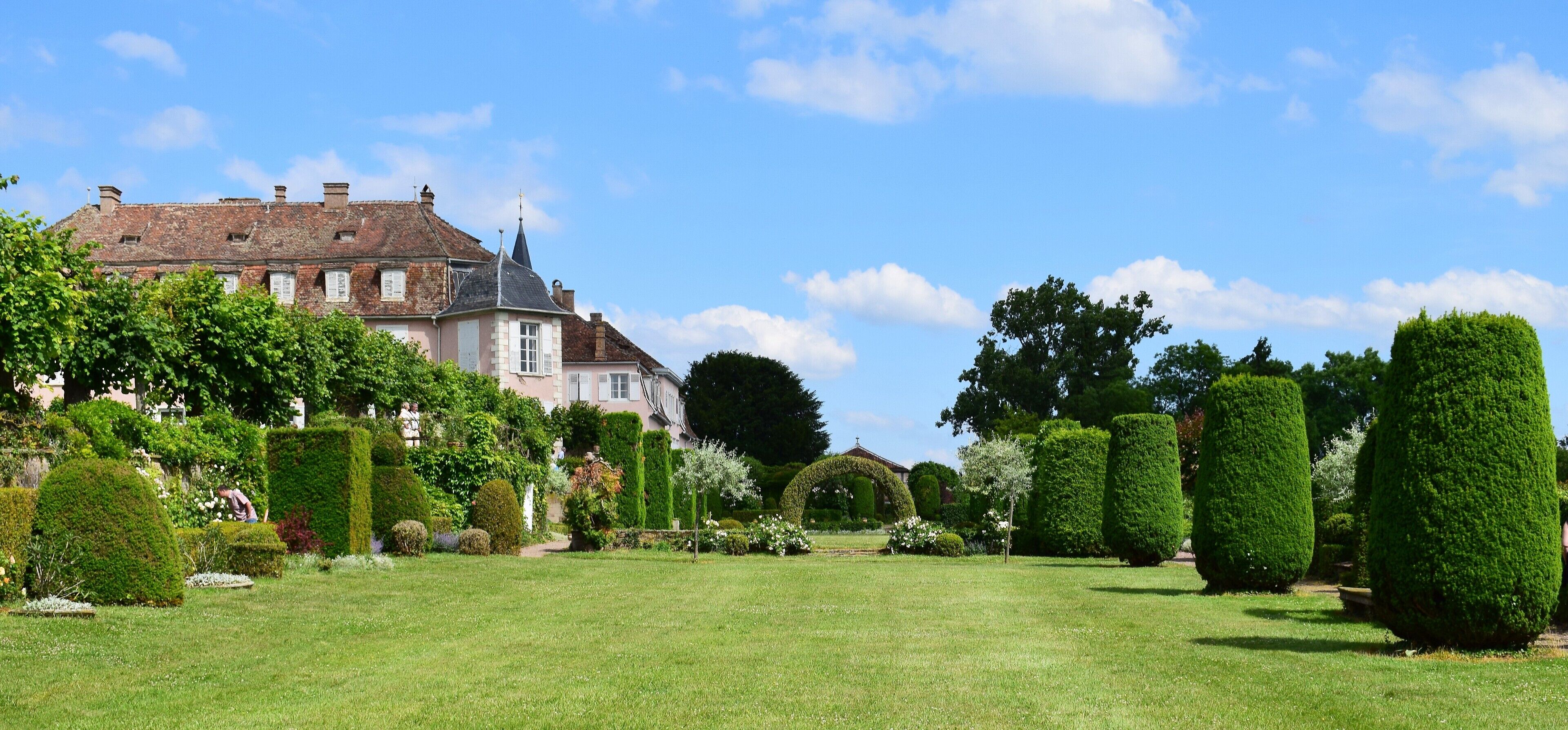 A large, historic house with a well-manicured garden, including neatly trimmed hedges and a variety of trees.