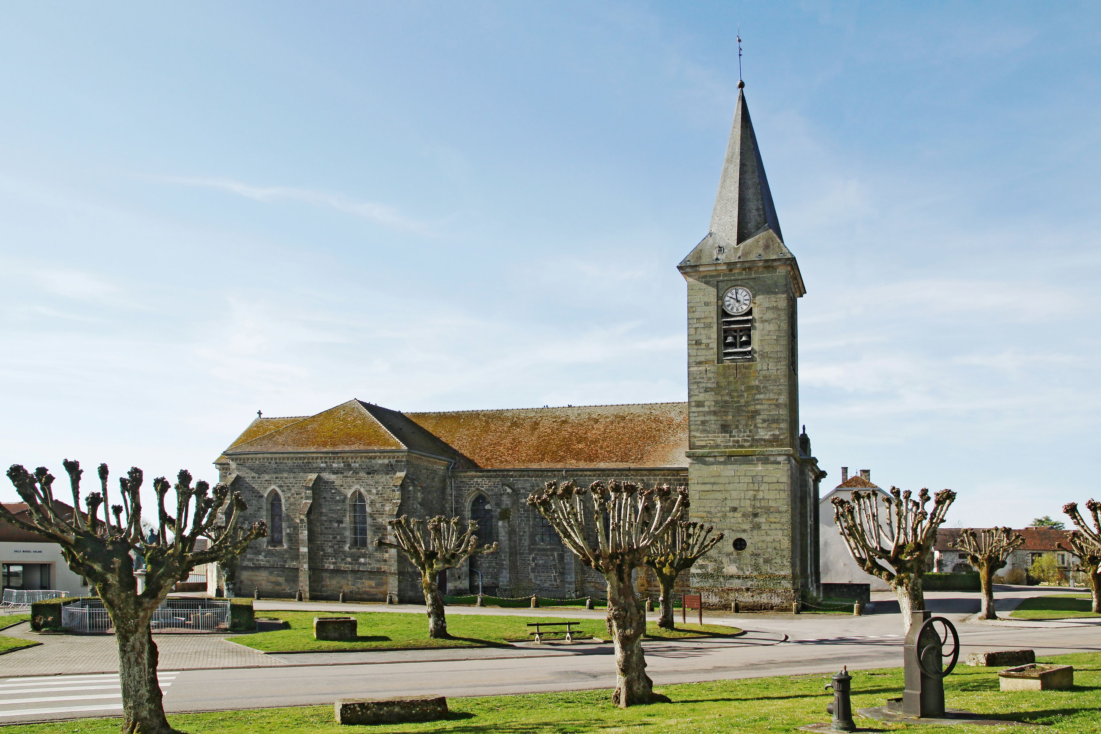 A historic church with a tall clock tower, surrounded by well-maintained trees and a paved walkway.