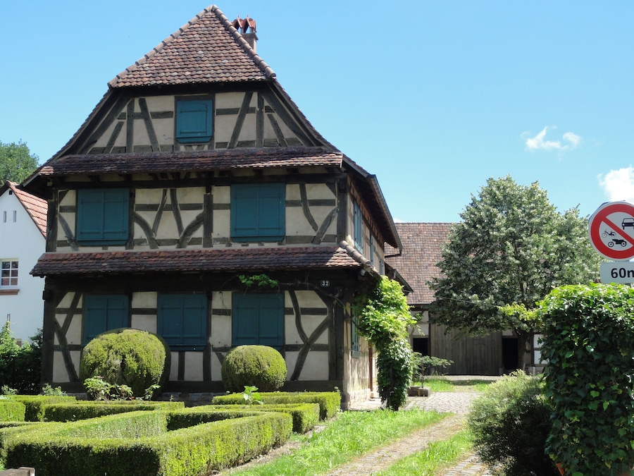 A traditional half-timbered house with a steep roof, surrounded by well-maintained hedges and a cobblestone path.