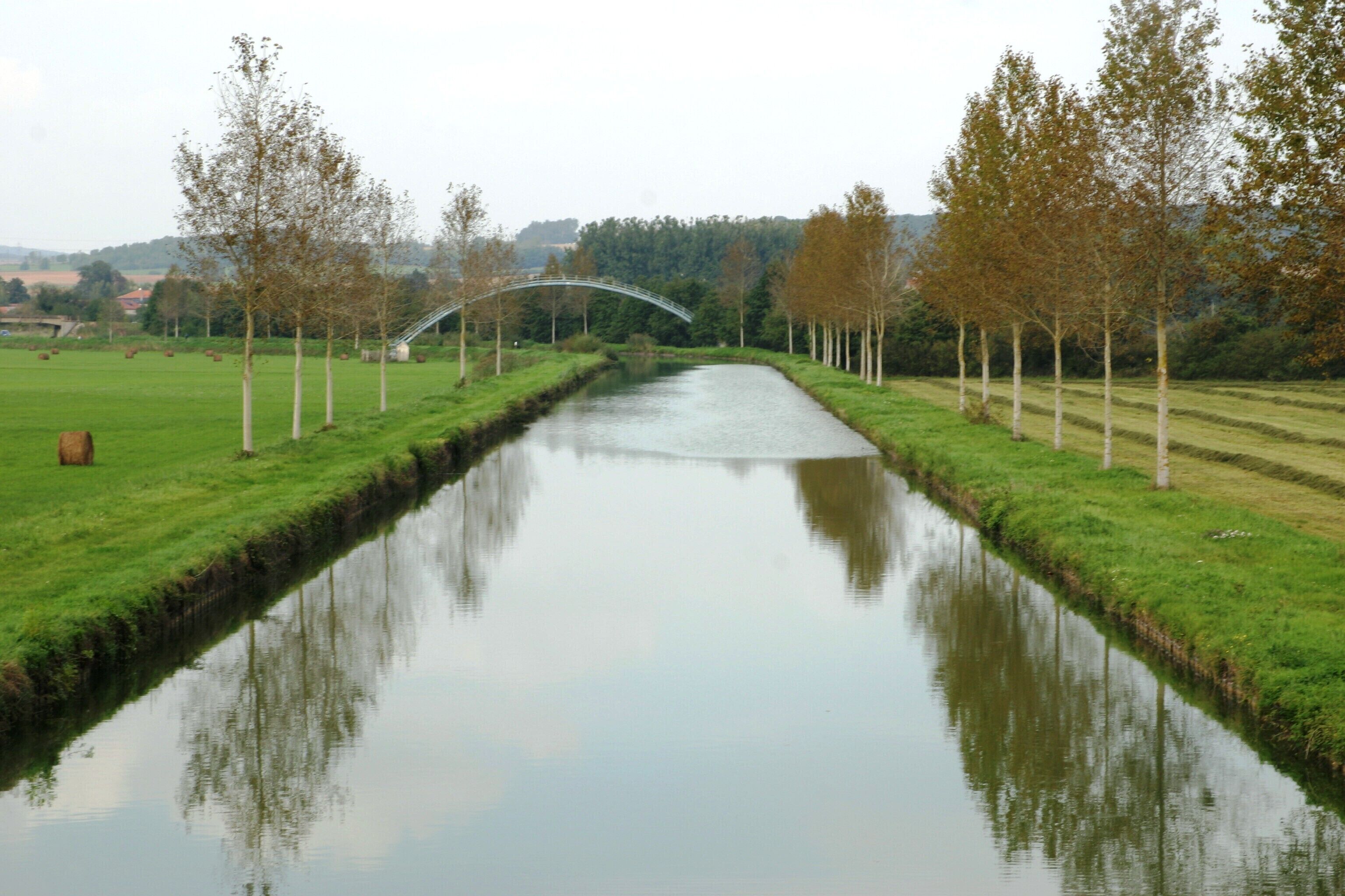A canal with a bridge, surrounded by trees and fields.