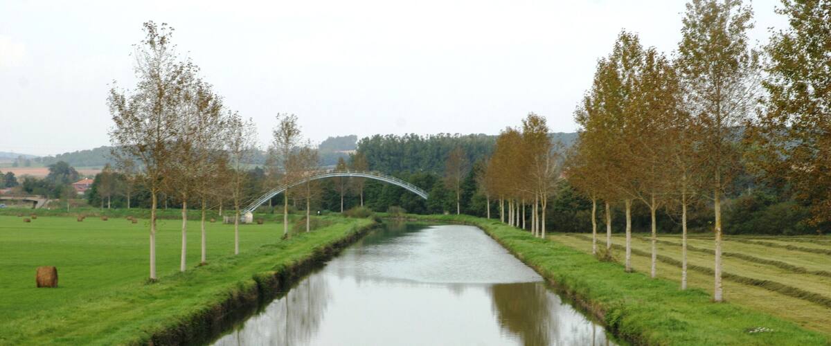 A canal with a bridge, surrounded by trees and fields.