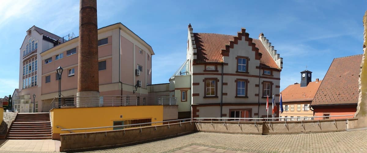 A cobblestone plaza with historic buildings, a tall chimney, and a yellow structure.