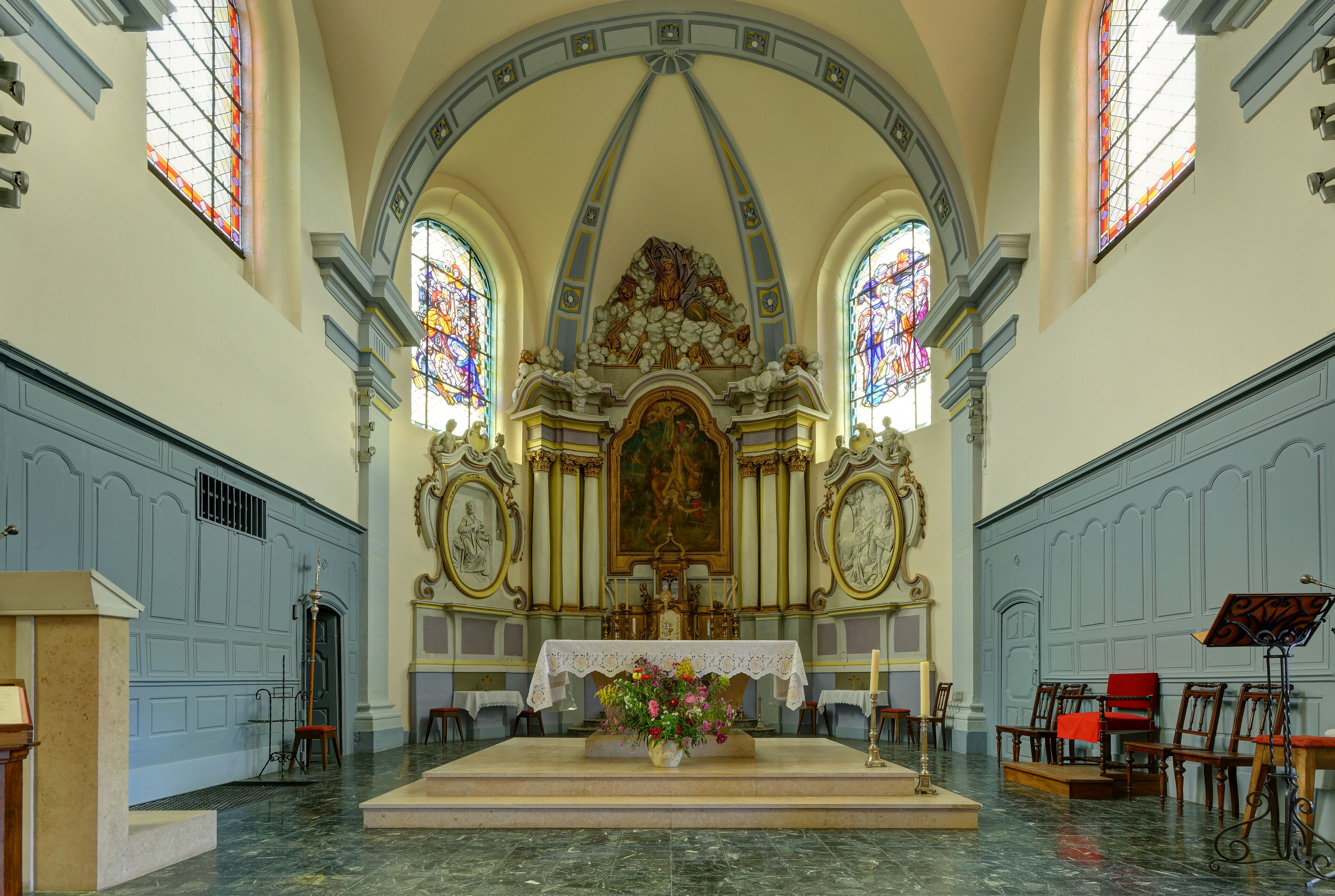 An ornate church interior with a central altar, stained glass windows, and classical architecture.