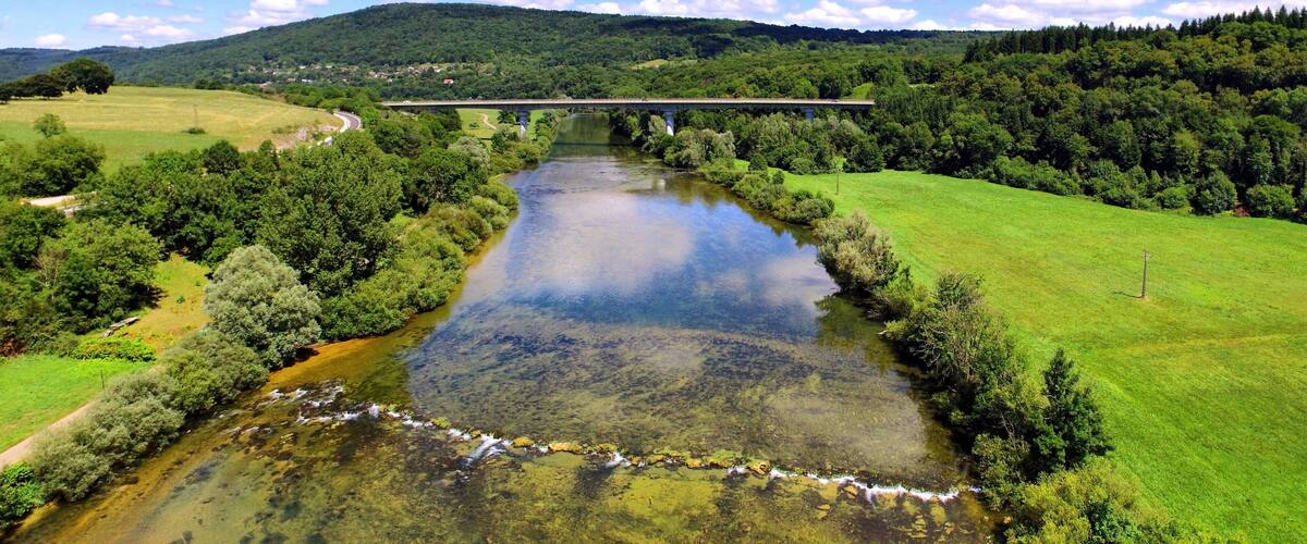 A river flowing through a valley with a bridge in the distance and a forested hillside.