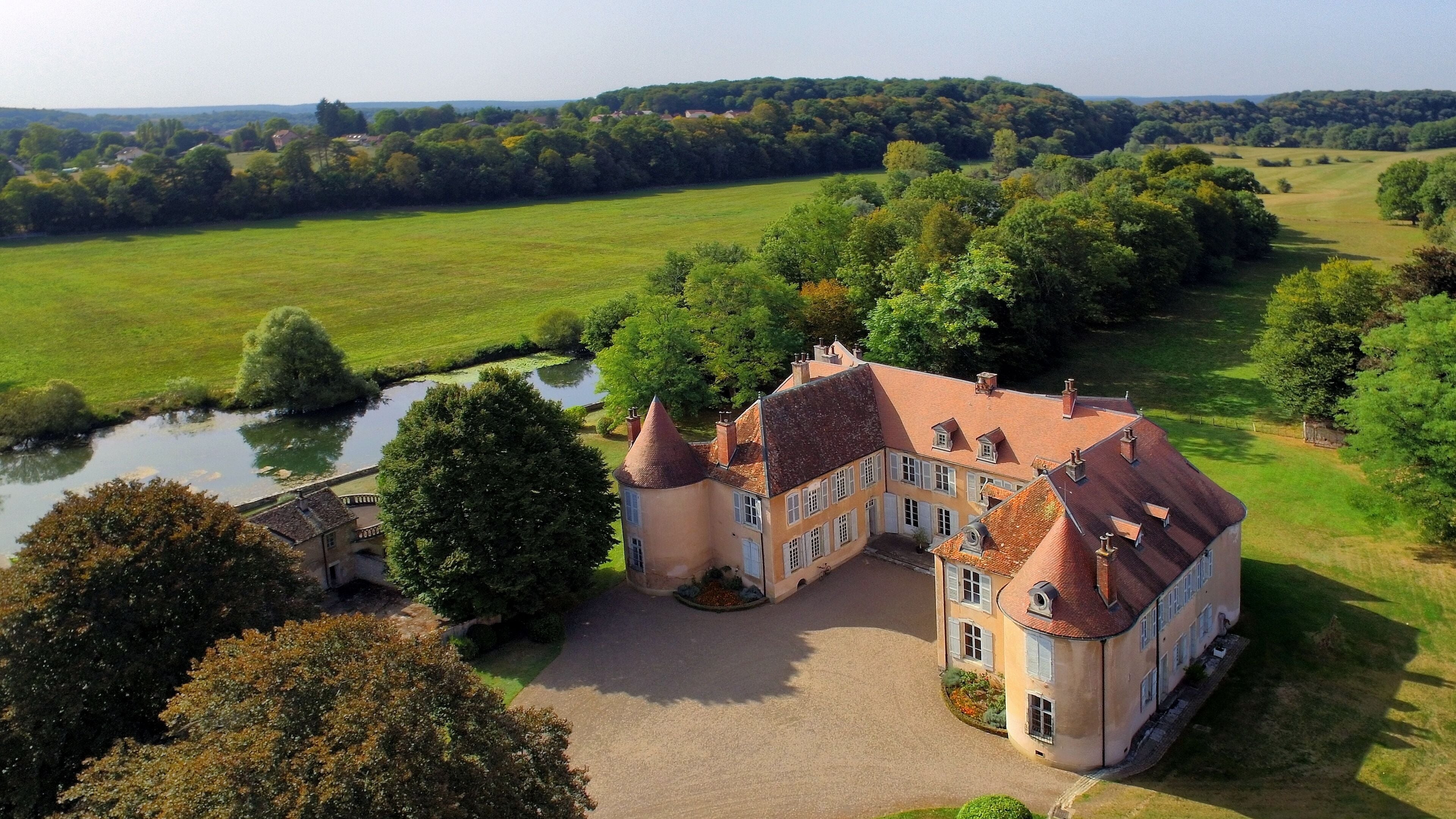 A large, historic estate with a river, lush greenery, and rolling hills in the background.