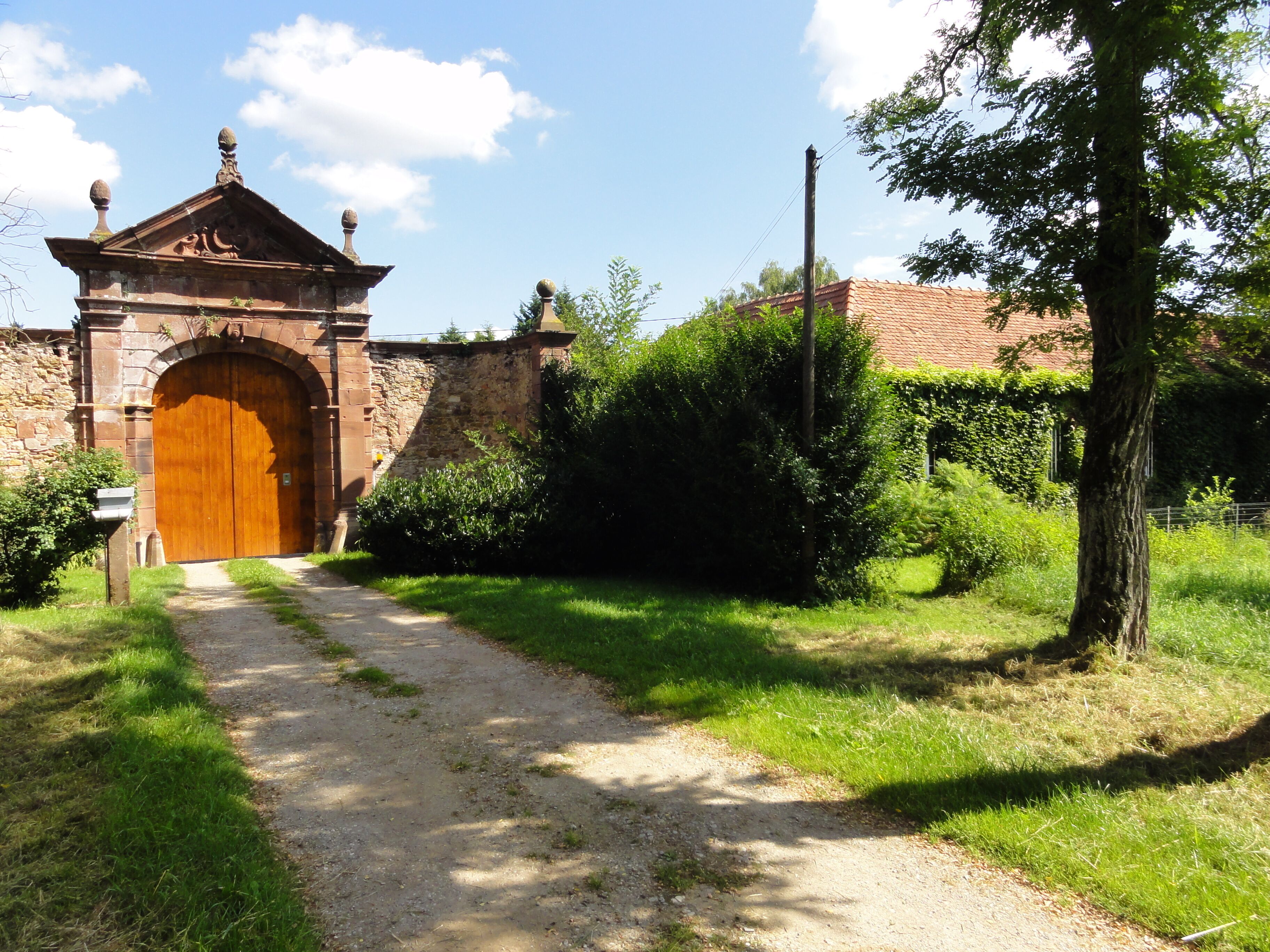 A stone archway with a wooden door, a dirt path, and greenery.