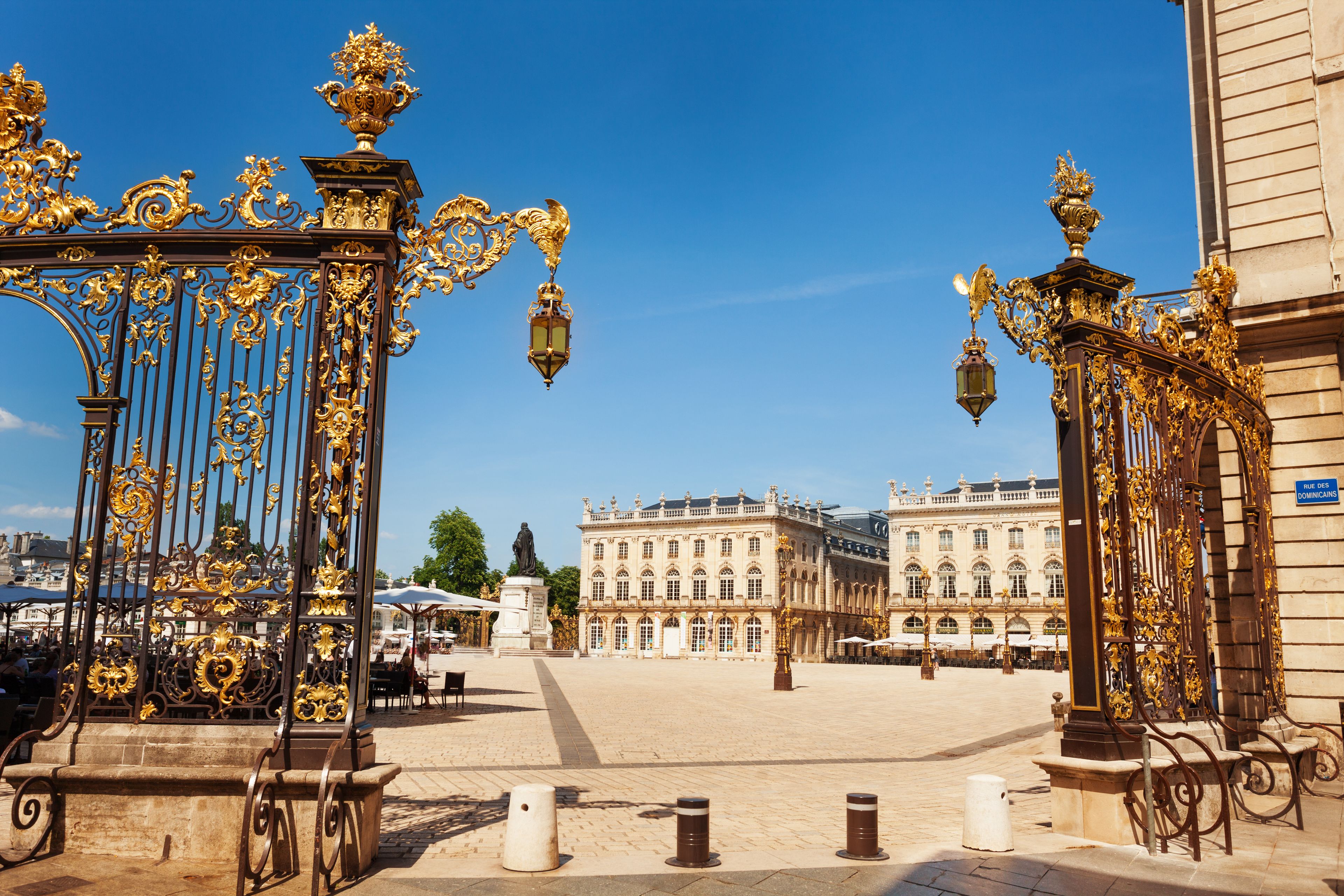 Verschnörkelte goldene Tore, eine Statue und ein historisches Gebäude mit wolkenlosem, blauem Himmel.