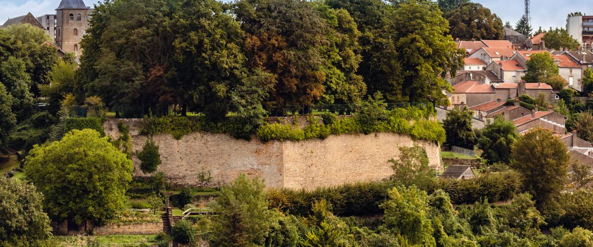 A historic town with a prominent church tower, lush greenery, and a stone wall.